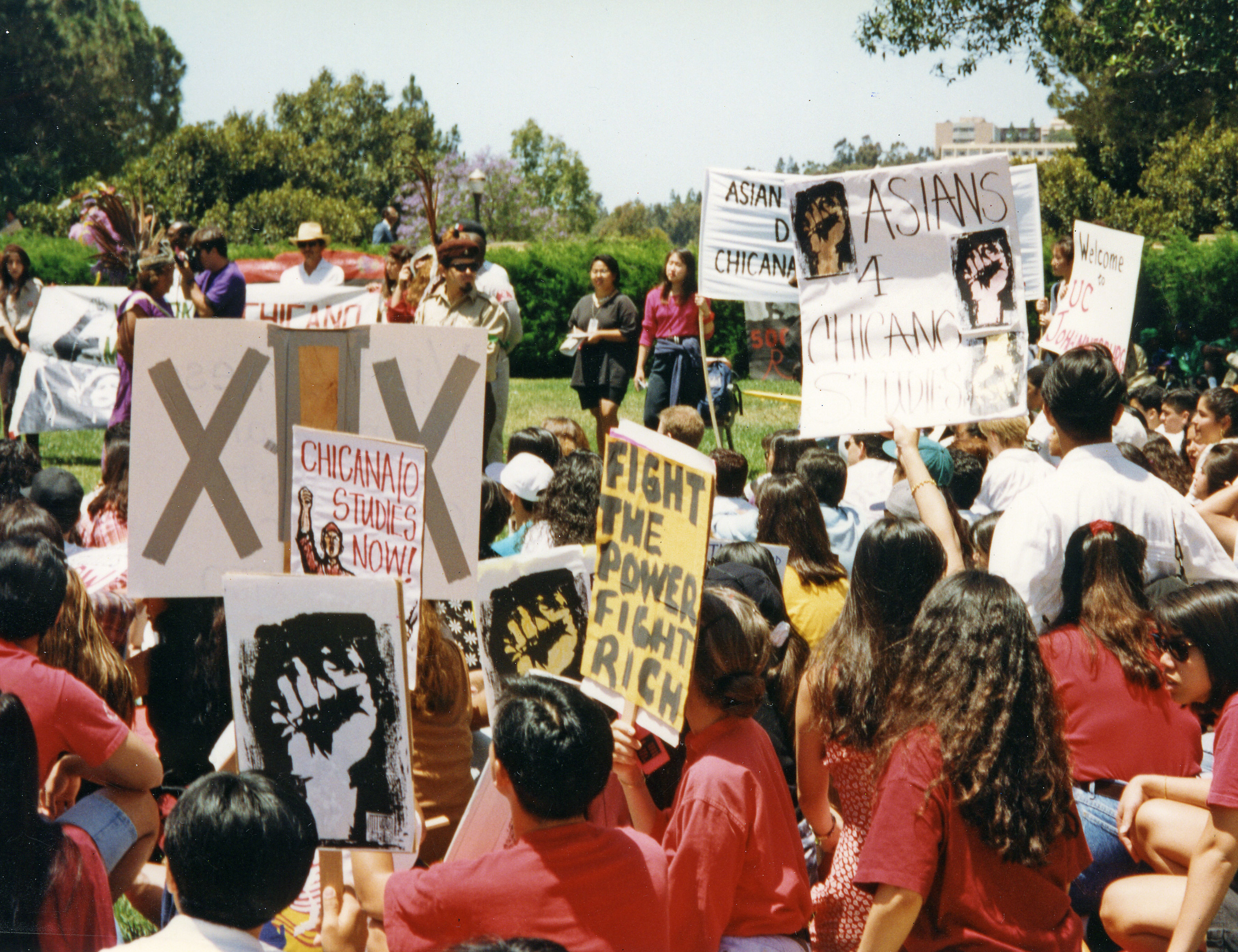 Speakers on a grassy hill address an audience holding protest signs