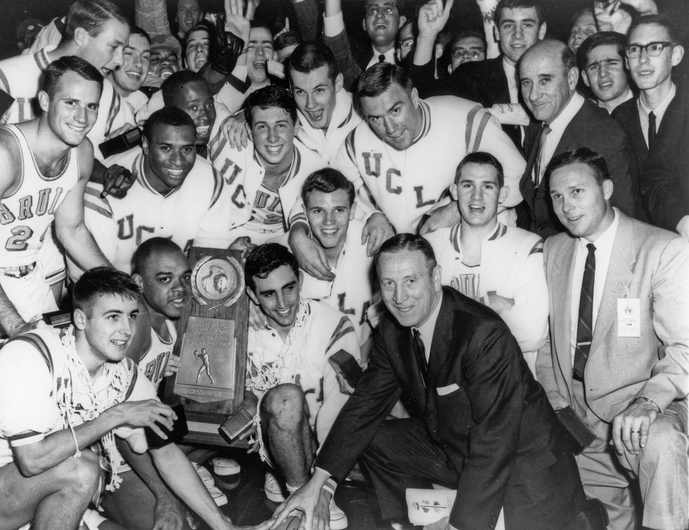 A team of basketball players and their coach gather around a trophy